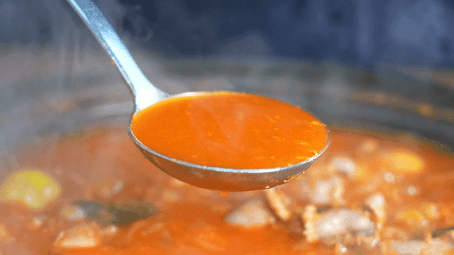 Ladle scooping out spicy chicken offal soup boiling in pot