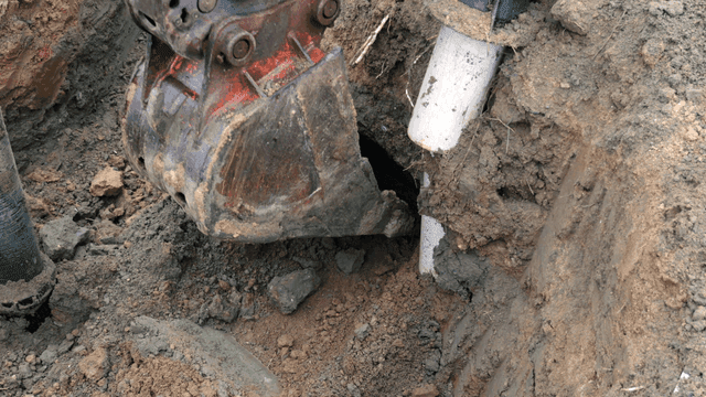 Excavator digging near a pipe in the soil