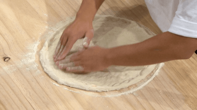 Hands rolling out dough on a cutting board