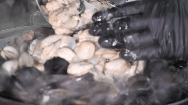 Oyster kalguksu being poured into pot in kitchen