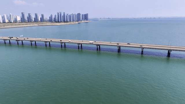 A long bridge over a vast sea with a city skyline