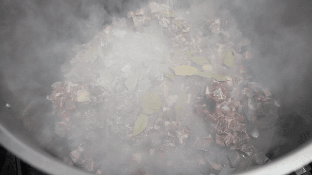 Salt and pepper sprinkled on meat and herbs boiling in pot