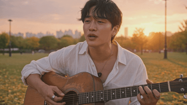 Man singing and playing guitar in park at sunset