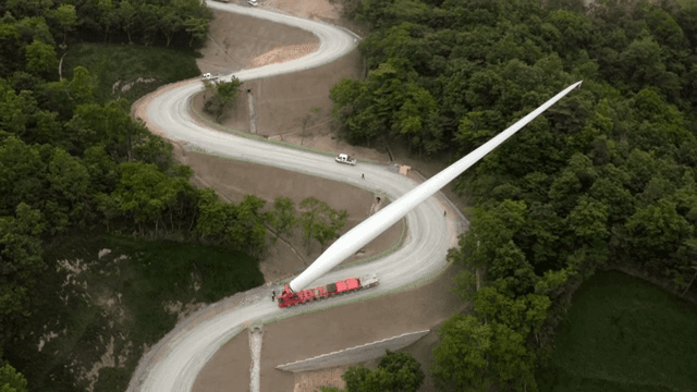 울창한 숲 속 구불구불한 도로에서 풍력 터빈 자재를 운반하는 모습