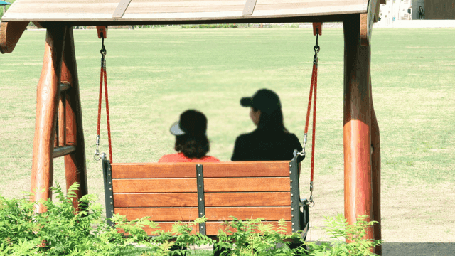 Two people sitting on a swing in a park