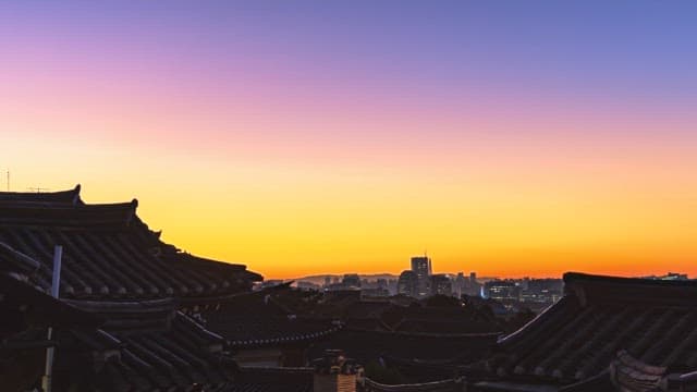 Sunrise over traditional rooftops against a city skyline