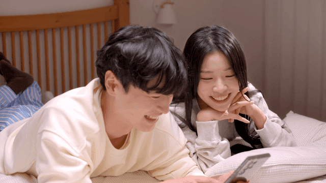 Couple smiling and talking while looking at phone in bed