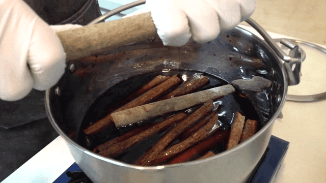 Adding cinnamon to large pot of red wine
