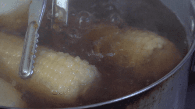 Corn boiling in a pot with tongs