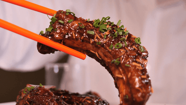 Chopsticks holding delicious marinated ribs garnished with herbs