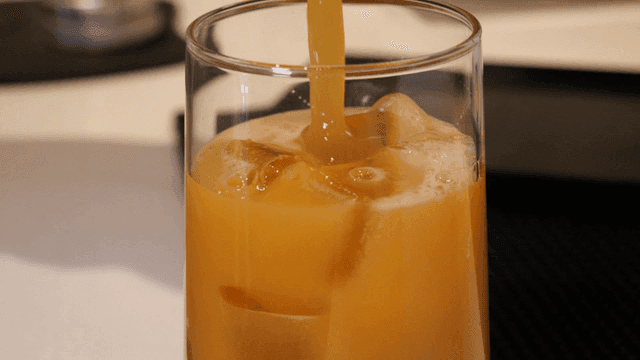Orange juice being poured into glass of ice