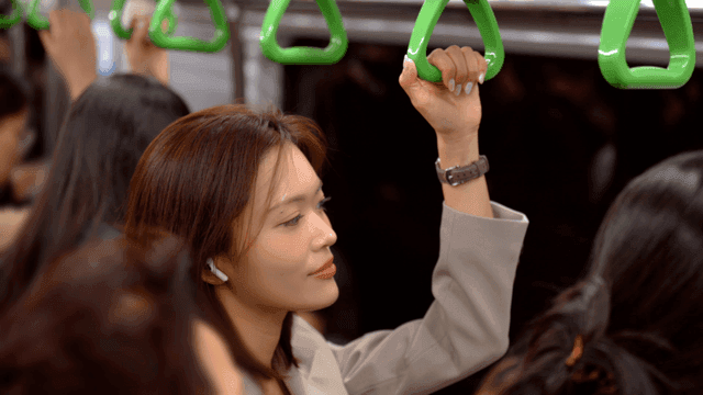 Woman holding onto handrail and listening to music through earphones in crowded subway