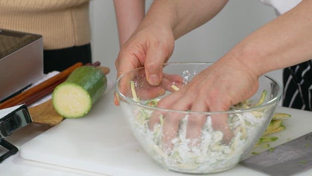 Mixing sliced ​​zucchini and flour in a glass bowl in the kitchen