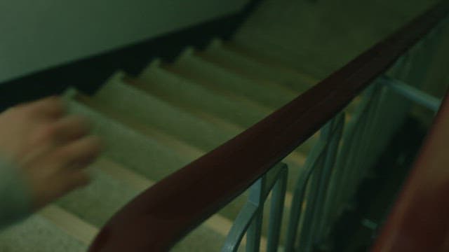 건물 복도의 어두운 조명 속 실내 계단을 내려가는 사람