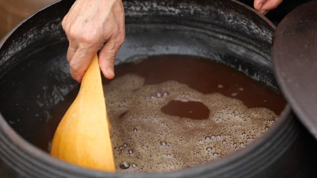 Pouring soy sauce intp a crock jar with a wooden ladle