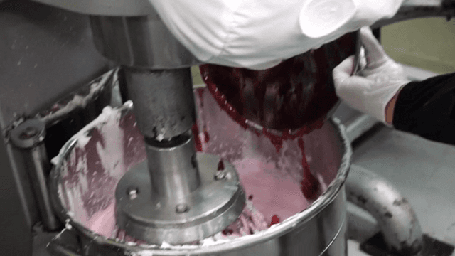 A person adding jam to a large dough mixer