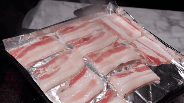 Sizzling frozen pork belly slices on a grill