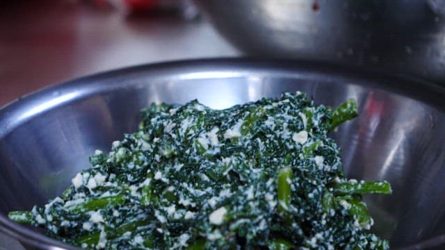 으깬 두부를 섞은 나물을 접시에 담는 사람