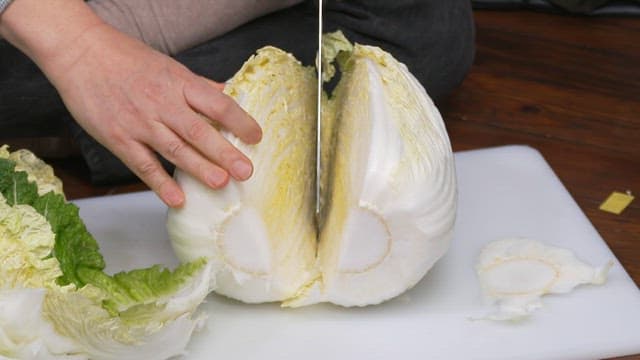 Person slicing a fresh cabbage with a knife on a cutting board