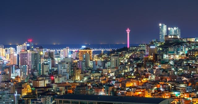 Bustling neiborhood at night with brightly lit buildings and a visible tower