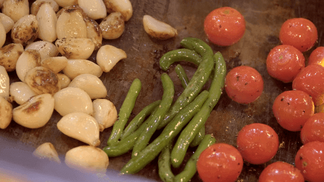 Torch flame grilling garlic, green beans, and cherry tomatoes on griddle