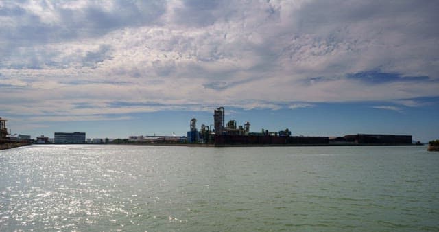 낮부터 저녁까지의 바다 근처에 위치한 산업단지 풍경