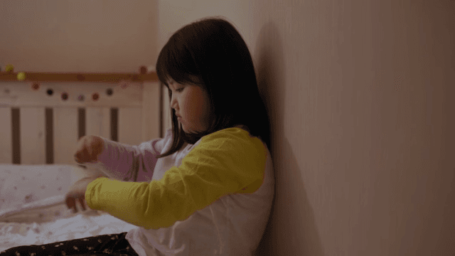 침대에 앉아 팔찌를 손목에 감아보는 아이