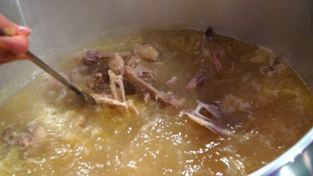 Stirring chicken soup in a large pot with ladle