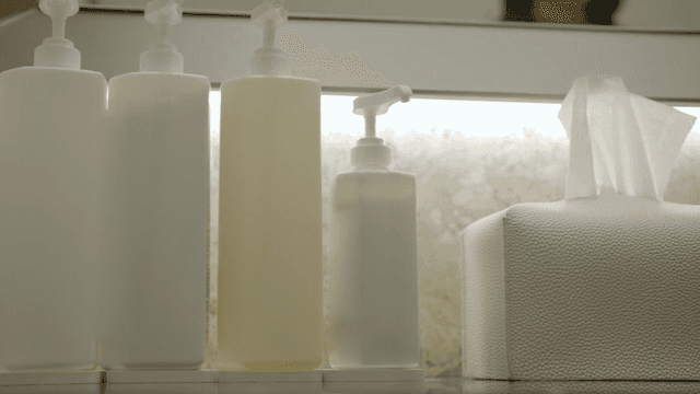 욕실에서 비누 디스펜서를 누르는 손