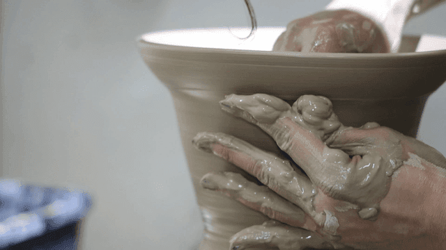 Hands shaping clay on a pottery wheel
