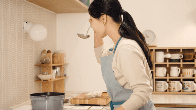 Woman tasting soup with ladle in cozy kitchen