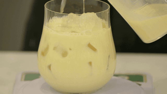 Pouring yellow drink into a glass with ice