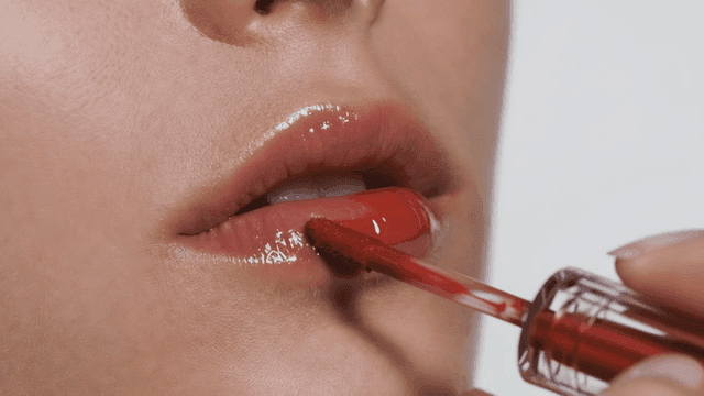 Woman applying red lip gloss to her lips