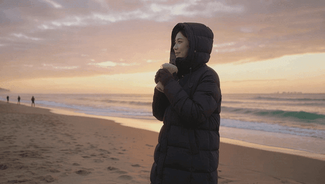 Woman wearing a long padded jacket at sunrise on the beach