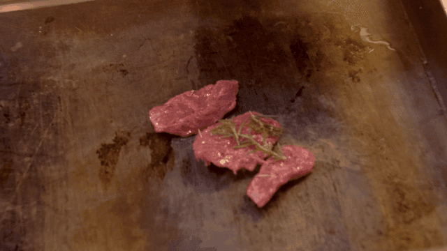 Raw meat topped with herbs on hot grill