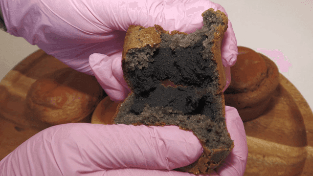 Hand wearing pink gloves splitting black muffin