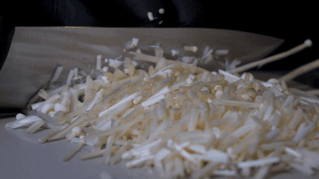 Enoki mushrooms being sliced on a board