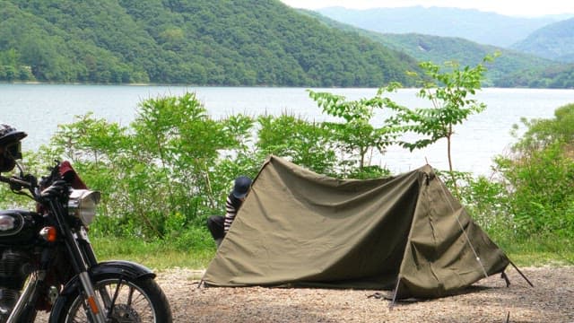 Man setting up a tent by a lake with vegetation on a clear day