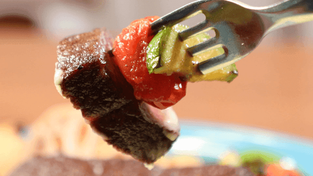 A fork holding grilled steak and vegetables