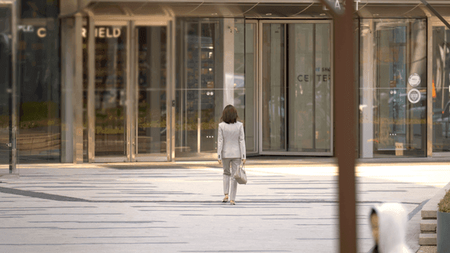 Back view of female office worker walking toward Hyundai Building
