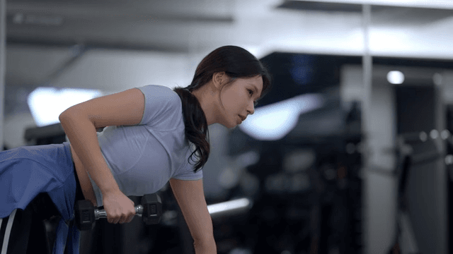 헬스장에서 덤벨 로우 운동을 하는 젊은 여성의 옆모습