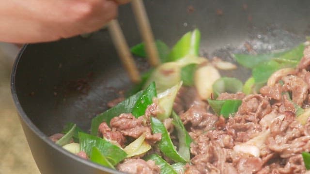 Stir-frying bulgogi with green onions using chopsticks in a frying pan