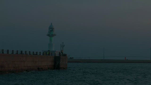 Lighthouse at dusk next to the beach with a pier