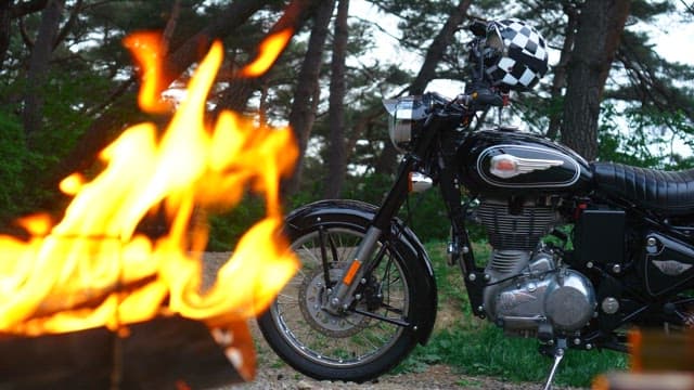 Lush forest with a roaring campfire and a black motorcycle