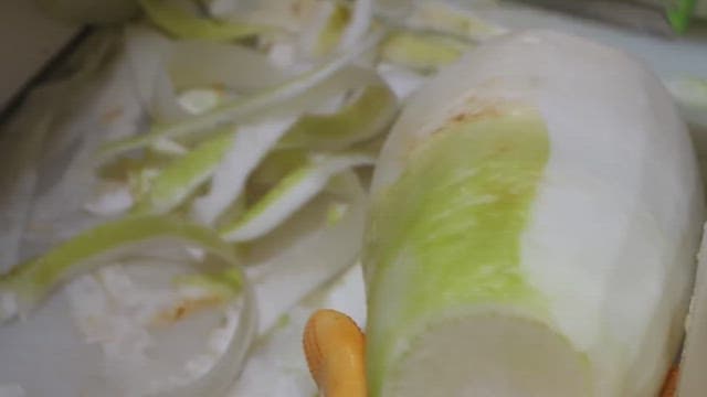 Hands wearing gloves peeling white radishes.