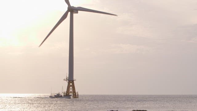 Wind turbines on the sea with a boat sailing at sunset