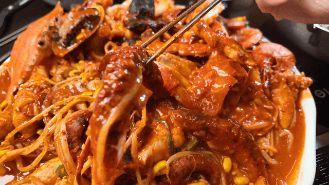 Chopsticks picking up spicy seafood stew containing crab and octopus