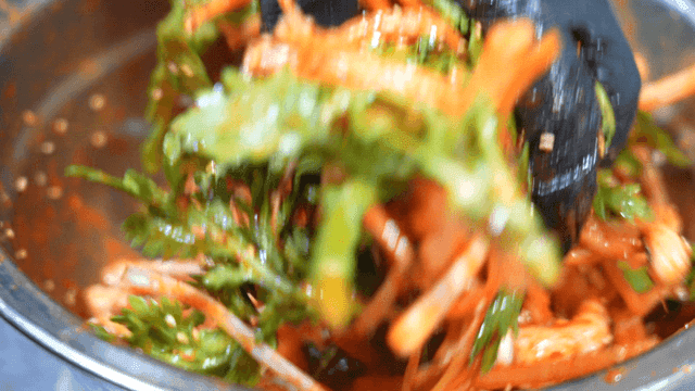 Hand mixing seasoned squid salad and vegetables in bowl