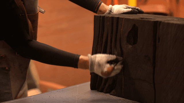 검게 탄 나무 조각품을 송곳으로 다듬는 공예가