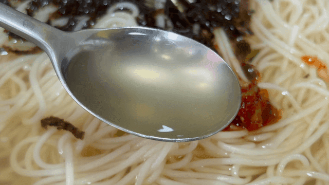 Lifting clear broth of seaweed and spice banquet noodles by spoon